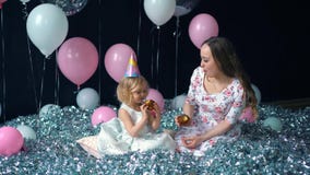 La niña linda y su mamá joven hermosa comen las magdalenas, fiesta de cumpleaños, celebración de días festivos En el fondo de glo almacen de video La niña linda y su mamá joven hermosa comen las magdalenas, fiesta de cumpleaños, celebración de días festivos En el fondo de glo almacen de video