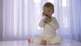 La niñez moderna, bebé divertido precioso es jugada y que habla en el teléfono móvil en sitio brillante metrajes La niñez moderna, bebé divertido precioso es jugada y que habla en el teléfono móvil en sitio brillante metrajes