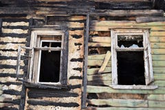 La pared dañada de la casa del fuego y de dos ventanas con el vidrio quebrado en los rayos del sol poniente en la primavera foto de archivo La pared dañada de la casa del fuego y de dos ventanas con el vidrio quebrado en los rayos del sol poniente en la primavera foto de archivo