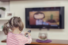 La pequeña muchacha linda con el telecontrol cambia el canal en la TV fotografía de archivo libre de regalías La pequeña muchacha linda con el telecontrol cambia el canal en la TV fotografía de archivo libre de regalías
