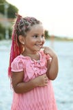 La petite fille bronzée mignonne avec la coiffure colorée de tresses portant une robe rose est très curieuse à la plage d'été Image libre de droits La petite fille bronzée mignonne avec la coiffure colorée de tresses portant une robe rose est très curieuse à la plage d'été Image libre de droits