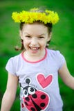 La petite fille dans une guirlande des pissenlits jaunes photographie stock libre de droits La petite fille dans une guirlande des pissenlits jaunes photographie stock libre de droits