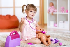 La petite fille joue le docteur examinant un patient de poupée photographie stock libre de droits La petite fille joue le docteur examinant un patient de poupée photographie stock libre de droits