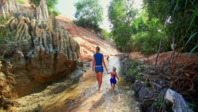 La petite fille marche à la main avec la mère le long du courant féerique La petite fille marche à la main avec la mère le long du courant féerique