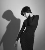 La ragazza che posa in un vestito elegante nero, getta un'ombra sulla parete fotografia stock La ragazza che posa in un vestito elegante nero, getta un'ombra sulla parete fotografia stock
