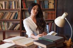 La ragazza che si siede alla tavola che legge un libro sta preparando per l'esame Fotografia Stock La ragazza che si siede alla tavola che legge un libro sta preparando per l'esame Fotografia Stock