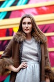 La ragazza dai capelli lunghi alla moda vestita in un vestito grigio ed in un cappotto di pelle di pecora marrone lungo posa nell immagini stock libere da diritti La ragazza dai capelli lunghi alla moda vestita in un vestito grigio ed in un cappotto di pelle di pecora marrone lungo posa nell immagini stock libere da diritti