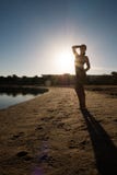 La ragazza dolce e snella sta sulla spiaggia contro il tramonto Siluetta di un nuotatore in un costume da bagno immagini stock La ragazza dolce e snella sta sulla spiaggia contro il tramonto Siluetta di un nuotatore in un costume da bagno immagini stock