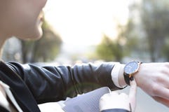 La ragazza esamina l'orologio, il sole sta splendendo nella macchina fotografica fotografie stock La ragazza esamina l'orologio, il sole sta splendendo nella macchina fotografica fotografie stock