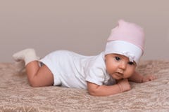 La ragazza neonata adorabile striscia sul letto, vestito in bello cappello rosa, sguardi innocente nella macchina fotografica Pic immagine stock libera da diritti La ragazza neonata adorabile striscia sul letto, vestito in bello cappello rosa, sguardi innocente nella macchina fotografica Pic immagine stock libera da diritti