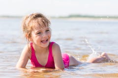La ragazza quinquennale si trova in acqua in secca del fiume, ridente e guardante a sinistra immagine stock libera da diritti La ragazza quinquennale si trova in acqua in secca del fiume, ridente e guardante a sinistra immagine stock libera da diritti