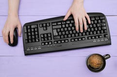 La ragazza stampa su una tastiera nera e tiene un topo Offee del ¡ di Ð con schiuma in tazza nera Fondo di legno viola fotografia stock libera da diritti La ragazza stampa su una tastiera nera e tiene un topo Offee del ¡ di Ð con schiuma in tazza nera Fondo di legno viola fotografia stock libera da diritti