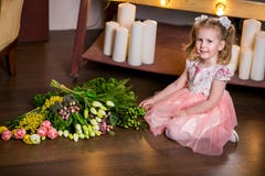 La ragazza sveglia favorita in un vestito rosa si siede sul pavimento accanto ad un mazzo dei tulipani, della mimosa, delle bacch immagini stock libere da diritti La ragazza sveglia favorita in un vestito rosa si siede sul pavimento accanto ad un mazzo dei tulipani, della mimosa, delle bacch immagini stock libere da diritti
