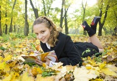 La ragazza teenager scrive la poesia in copybook nella sosta di autunno fotografia stock La ragazza teenager scrive la poesia in copybook nella sosta di autunno fotografia stock