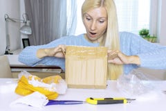 La seduta e l'apertura bionde emozionanti della donna una scatola, un pacchetto, oggetti sulla tavola sono nel disordine immagini stock libere da diritti La seduta e l'apertura bionde emozionanti della donna una scatola, un pacchetto, oggetti sulla tavola sono nel disordine immagini stock libere da diritti