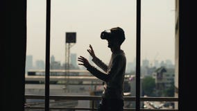 La silhouette du film de observation de jeune homme dans le casque de VR et ont l'expérience de réalité virtuelle sur le balcon d images stock La silhouette du film de observation de jeune homme dans le casque de VR et ont l'expérience de réalité virtuelle sur le balcon d images stock