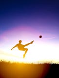 La silueta del jugador de fútbol golpea la bola con el pie Fotografía de archivo La silueta del jugador de fútbol golpea la bola con el pie Fotografía de archivo