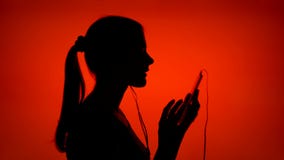 La siluetta della giovane donna messa sui trasduttori auricolari ed ascolta musica sullo Smart Phone su fondo rosso archivi video La siluetta della giovane donna messa sui trasduttori auricolari ed ascolta musica sullo Smart Phone su fondo rosso archivi video