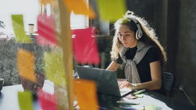 La studentessa attraente sta ascoltando musica con le cuffie che ballano e che cantano mentre lavorava con il computer portatile stock footage La studentessa attraente sta ascoltando musica con le cuffie che ballano e che cantano mentre lavorava con il computer portatile stock footage