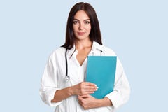La taille a tiré du docteur féminin tient le dossier bleu, prêt à examiner des patients, porte l'uniforme médical, regarde sérieu image libre de droits La taille a tiré du docteur féminin tient le dossier bleu, prêt à examiner des patients, porte l'uniforme médical, regarde sérieu image libre de droits