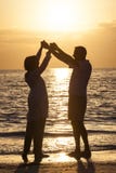 La tenuta senior delle coppie passa al tramonto la spiaggia tropicale fotografia stock La tenuta senior delle coppie passa al tramonto la spiaggia tropicale fotografia stock