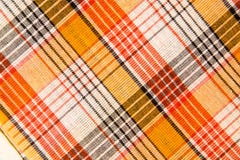 La textura de la tela de algodón a cuadros, anaranjada, roja, negra blanca Fotos de archivo libres de regalías La textura de la tela de algodón a cuadros, anaranjada, roja, negra blanca Fotos de archivo libres de regalías