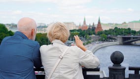 La vista trasera de pares mayores se coloca en mirada de la plataforma de observación alrededor de ciudad Viaje de los pensionist almacen de metraje de vídeo La vista trasera de pares mayores se coloca en mirada de la plataforma de observación alrededor de ciudad Viaje de los pensionist almacen de metraje de vídeo
