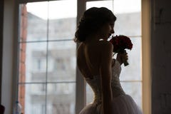 La vue arrière de la silhouette de jeune mariée près de la fenêtre sent les fleurs rouges image libre de droits La vue arrière de la silhouette de jeune mariée près de la fenêtre sent les fleurs rouges image libre de droits