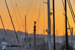 La vue de silhouette de statue de Columbus par des arbres et des linceuls des bateaux a amarré dans le port au coucher du soleil photo stock La vue de silhouette de statue de Columbus par des arbres et des linceuls des bateaux a amarré dans le port au coucher du soleil photo stock
