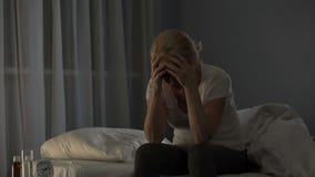 Lady sitting on bed, unable to fall asleep due to severe migraine and bad pain
