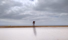landschap van een strand met bewolkte hemel en een lange badmeesterpost met groene vlag bij het midden Eerst heeft het zeewater royalty-vrije stock foto landschap van een strand met bewolkte hemel en een lange badmeesterpost met groene vlag bij het midden Eerst heeft het zeewater royalty-vrije stock foto