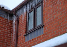 Lange Eiszapfen hängen von der Gosse eines Hauses Das Dach wird im Schnee bedeckt und es schneit noch stockfotografie Lange Eiszapfen hängen von der Gosse eines Hauses Das Dach wird im Schnee bedeckt und es schneit noch stockfotografie