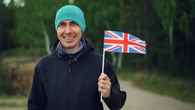 Langzaam motieportret van het glimlachen van van de de sportenventilator van Engelsman de holdings Britse vlag die in de wind vli stock video Langzaam motieportret van het glimlachen van van de de sportenventilator van Engelsman de holdings Britse vlag die in de wind vli stock video
