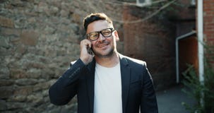 Langzame motie van het gelukkige zakenman spreken op mobiele telefoon die in openlucht glimlachen stock video Langzame motie van het gelukkige zakenman spreken op mobiele telefoon die in openlucht glimlachen stock video