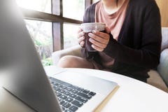 Laptop und Kaffeetasse in den Händen des Mädchens, die zu Hause sitzen lizenzfreie stockfotografie Laptop und Kaffeetasse in den Händen des Mädchens, die zu Hause sitzen lizenzfreie stockfotografie