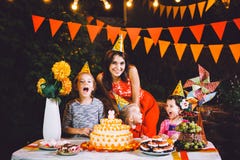 A large mother and three children at a festive table with sweets and a cake in the courtyard decorated with lights and a garland o royalty free stock photos A large mother and three children at a festive table with sweets and a cake in the courtyard decorated with lights and a garland o royalty free stock photos