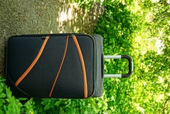 A large suitcase on wheels standing on a path near the green vegetation. Travelling black suitcase on the road near bushes and grass Royalty Free Stock Photos A large suitcase on wheels standing on a path near the green vegetation. Travelling black suitcase on the road near bushes and grass Royalty Free Stock Photos