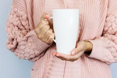 A large white cup for coffee or tea in the hands of a young woman dressed in a knitted cardigan of peach color royalty free stock photography A large white cup for coffee or tea in the hands of a young woman dressed in a knitted cardigan of peach color royalty free stock photography