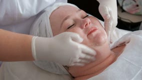 Las manos de un cosmetologist profesional aplicar una crema de alimentación o que rejuvenece en el cuello y la cara de una mujer almacen de metraje de vídeo Las manos de un cosmetologist profesional aplicar una crema de alimentación o que rejuvenece en el cuello y la cara de una mujer almacen de metraje de vídeo