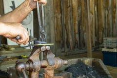 Las manos del ` s del herrero en el trabajo en la fragua que trabajaba con el objeto se sostuvieron en tornillo con las pinzas en foto de archivo Las manos del ` s del herrero en el trabajo en la fragua que trabajaba con el objeto se sostuvieron en tornillo con las pinzas en foto de archivo
