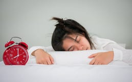 Las mujeres asiáticas duermen en la cama con el despertador por la mañana encendido fotos de archivo Las mujeres asiáticas duermen en la cama con el despertador por la mañana encendido fotos de archivo