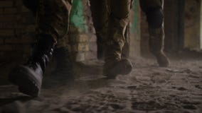 Las piernas del soldado en botas de combate del ejército caminan en el edificio almacen de metraje de vídeo Las piernas del soldado en botas de combate del ejército caminan en el edificio almacen de metraje de vídeo