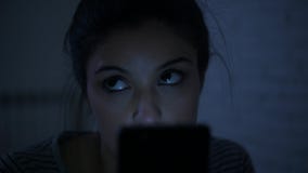 Lateral panning shot of young attractive hispanic woman on her 30s lying in bed late night using mobile phone look