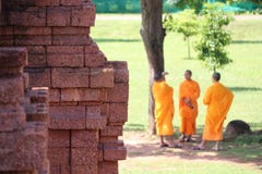 Lateritestenen av grunden av den huvudsakliga stupaen på Khao Klang Nok och fokuserar ut tre thailändska munkar som står under tr fotografering för bildbyråer Lateritestenen av grunden av den huvudsakliga stupaen på Khao Klang Nok och fokuserar ut tre thailändska munkar som står under tr fotografering för bildbyråer