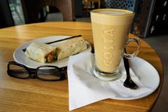 Latte del café de la marca de la costa, bocadillo del desayuno y vidrios de lectura americanos foto de archivo libre de regalías Latte del café de la marca de la costa, bocadillo del desayuno y vidrios de lectura americanos foto de archivo libre de regalías