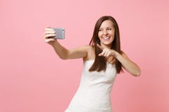 Laughing bride woman in white wedding dress pointing index finger on camera doing taking selfie shot on mobile phone