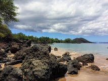 Lava Rock y coral con el espray de la onda que se estrella en piscinas de la marea en la playa de Maluaka y Kihei Maui con el cie Imagenes de archivo Lava Rock y coral con el espray de la onda que se estrella en piscinas de la marea en la playa de Maluaka y Kihei Maui con el cie Imagenes de archivo
