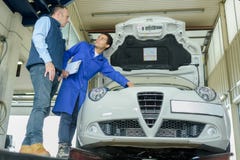 Lavoratori sorridenti che riparano il motore di automobile in garage immagini stock libere da diritti Lavoratori sorridenti che riparano il motore di automobile in garage immagini stock libere da diritti