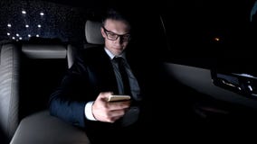 Le affärsmannen som kontrollerar mejl, genom att använda telefonen som sitter på baksätet av bilen royaltyfri fotografi Le affärsmannen som kontrollerar mejl, genom att använda telefonen som sitter på baksätet av bilen royaltyfri fotografi