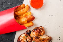 Le ali di pollo fritto con le patate al forno ed il bbq sauce sulla carta del mestiere su fondo nero immagine stock libera da diritti Le ali di pollo fritto con le patate al forno ed il bbq sauce sulla carta del mestiere su fondo nero immagine stock libera da diritti